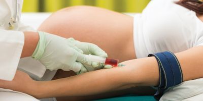 Torso of a pregnant woman. Her arm is being injected with a red fluid, by a hand in latex gloves