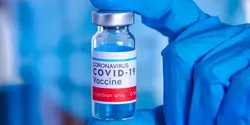 A gloved hand holding a vial of COVID-19 vaccine