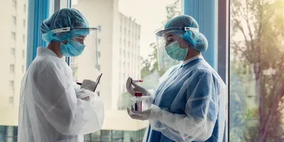 Two clinical workers wearing PPE and holding blood samples in a hospital