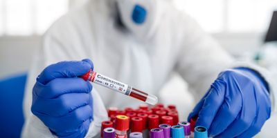 Clinical worker wearing PPE handling a blood sample labeled COVID-19