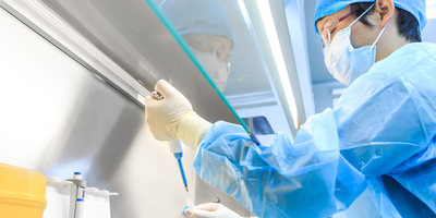 A laboratory researcher wearing PPE holding a pipette in a biological safety cabinet