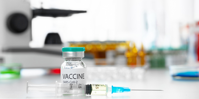 A glass vial of COVID-19 vaccine on a table next to a syringe