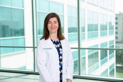 A photo of researcher Maria Chahrour, Ph.D. in a white lab coat standing by the window
