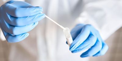 A person wearing personal protective equipment putting a nasal SARS-CoV-2 swab into a tube