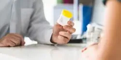 A clinical professional holding a urine cup out to a patient
