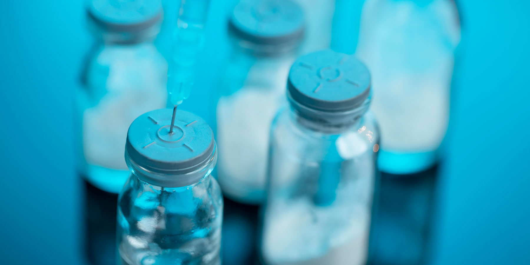Photo of syringe piecing the top of a glass COVID-19 mRNA vaccine vial