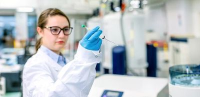 A female KAUST researcher wearing glasses and PPE holdings up a tube in a scientific lab.