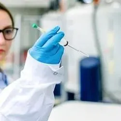 A female KAUST researcher wearing glasses and PPE holdings up a tube in a scientific lab.
