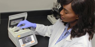 A Black laboratory professional wearing PPE loads a malaria sample into the Gazelle diagnostic test