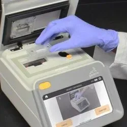 A Black laboratory professional wearing PPE loads a malaria sample into the Gazelle diagnostic test