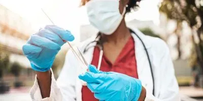 Black woman laboratory professional wearing PPE places a nasopharyngeal covid-19 swab sample into a sterile tube