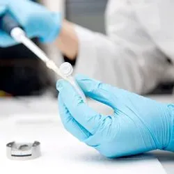 Photo of lab professional wearing PPE pipetting tumor sample into tube for whole genome analysis
