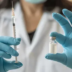 Photo of a clinical lab professional wearing PPE blue gloves holding up a vial of insulin and a syringe