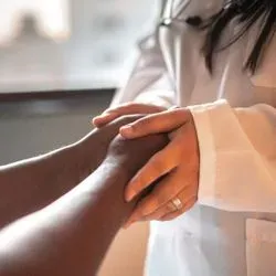 A female physician holds the hand of a multiple sclerosis patient