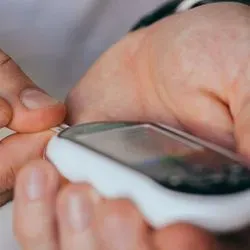 Photo of a white person taking a blood sugar test with a glucose monitor