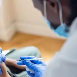 Photo of a Black clinician wearing PPE administering a vaccine to a Black five-year-old boy.