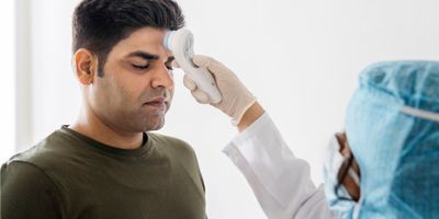 A clinical worker holds a temperature sensor to the forehead of a health care worker