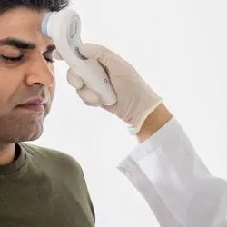 A clinical worker holds a temperature sensor to the forehead of a health care worker
