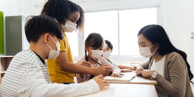 Photo of children wearing surgical masks and sitting at a table drawing