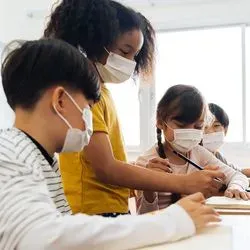 Photo of children wearing surgical masks and sitting at a table drawing