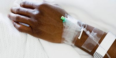 Photo of a Black COVID-19 patient with an IV line to receive monoclonal antibody therapy