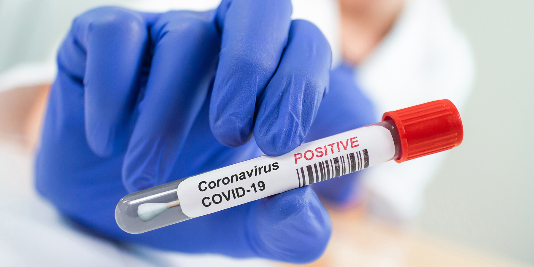 Photo of a coronavirus nasal swab being held in a hand wearing PPE