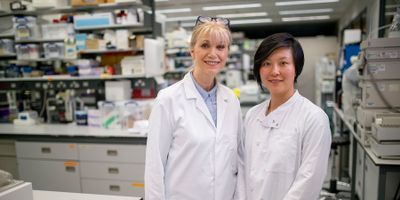 Two lab professionals wearing white lab coats standing side by side in the lab