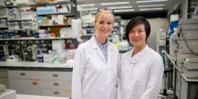 Two lab professionals wearing white lab coats standing side by side in the lab