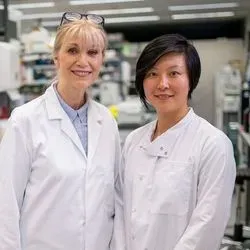 Two lab professionals wearing white lab coats standing side by side in the lab