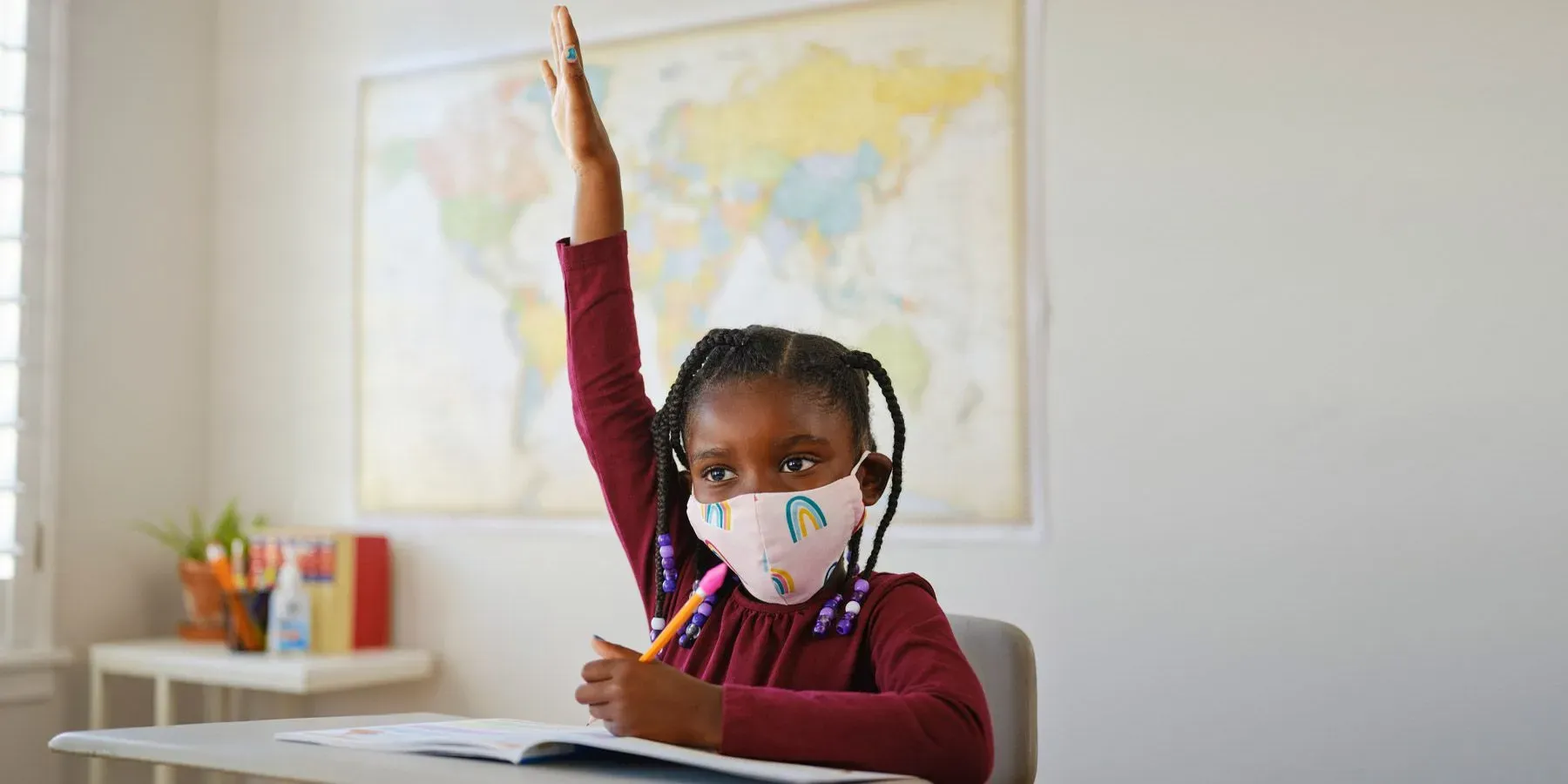 Child in school asking a question with hand up and wearing a mask