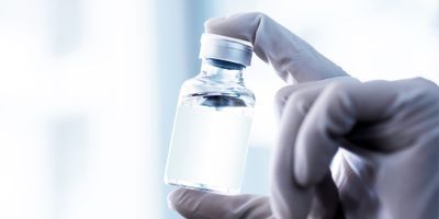 Photo of a lab professional holding up a vial of vaccine stored at ultra-low temperatures