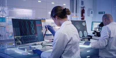 A lab professional wearing PPE is sitting at a computer doing quality management