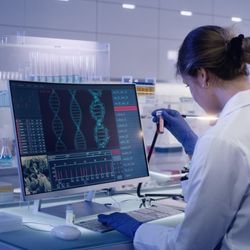 A lab professional wearing PPE is sitting at a computer doing quality management