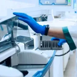 A laboratory worker wearing PPE handles automated hematology equipment