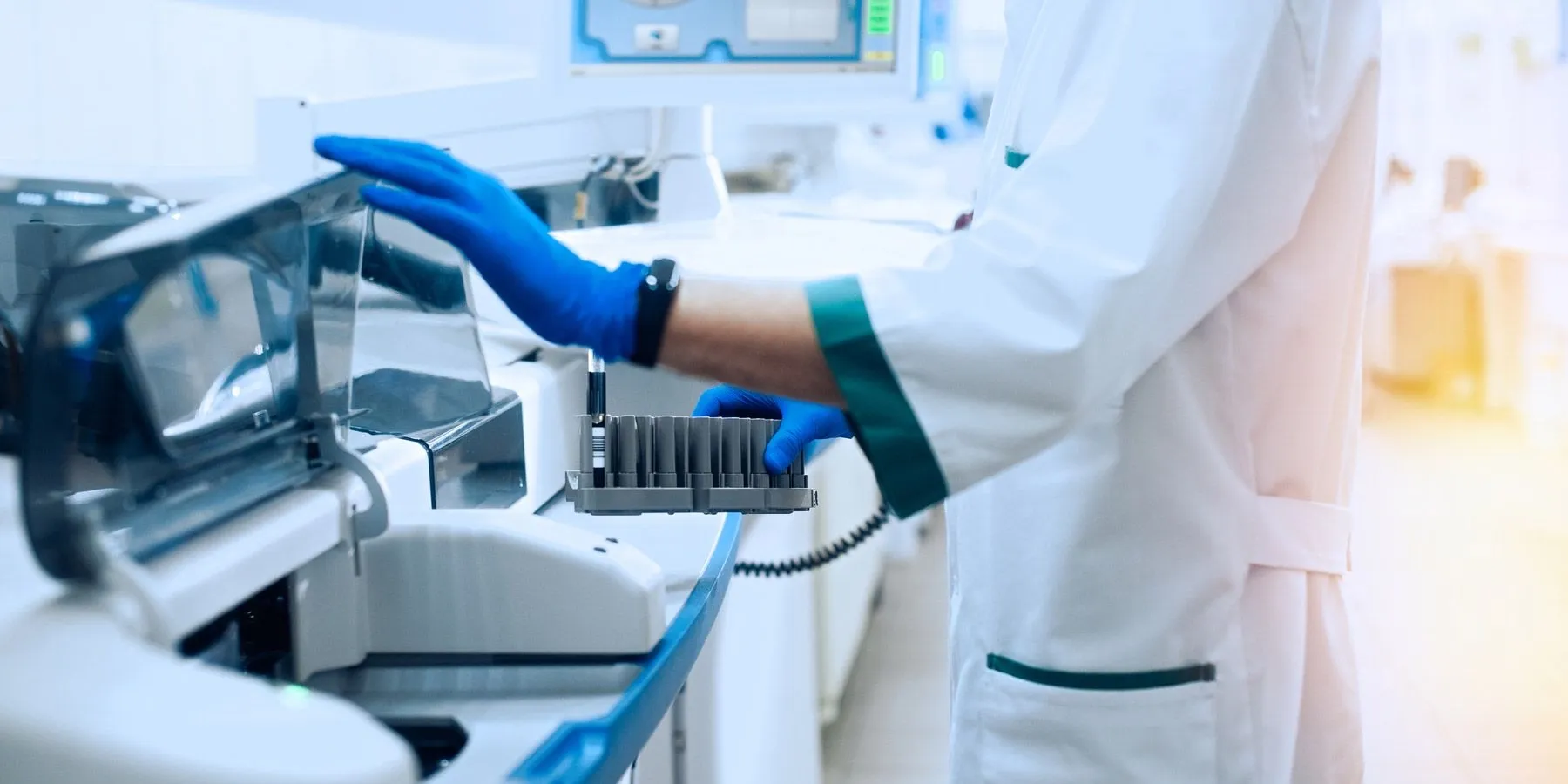 A laboratory worker wearing PPE handles automated hematology equipment
