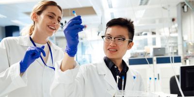 Two clinical lab professionals wearing PPE holding up a test tube in the lab