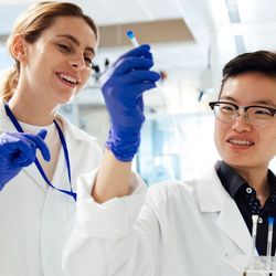 Two clinical lab professionals wearing PPE holding up a test tube in the lab