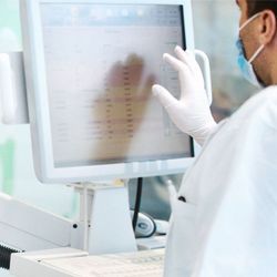 A clinical laboratory professional wearing PPE uses an automated lab terminal