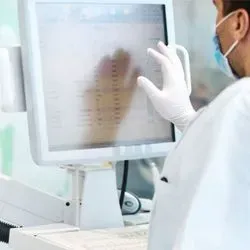 A clinical laboratory professional wearing PPE uses an automated lab terminal