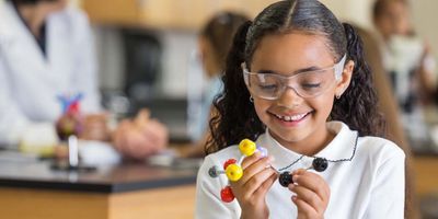 Photo of a Black child wearing protective eyewear holding a molecular model in their hands