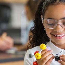 Photo of a Black child wearing protective eyewear holding a molecular model in their hands