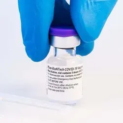 Gloved hand grabing a bottle of the COVID-19 vaccine