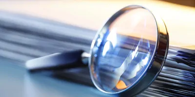Image of a magnifying glass leaning against a stack of papers