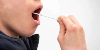 A patient swabs their cheek for a COVID-19 and influenza test.