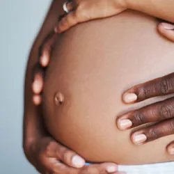 Photo of a pregnant belly with hands wrapped around it.