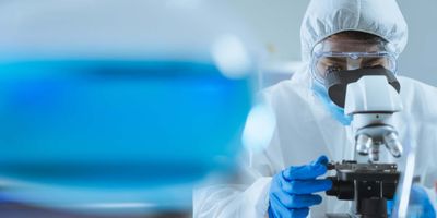 Researcher in full PPE looking down a microscope