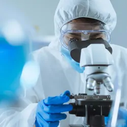 Researcher in full PPE looking down a microscope