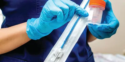 Photo of a health care provider wearing PPE holding a Pap smear test kit in their hands
