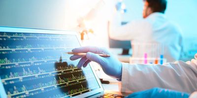 Researcher wearing gloves pointing at a computer screen with genetic information on it