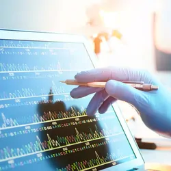 Researcher wearing gloves pointing at a computer screen with genetic information on it